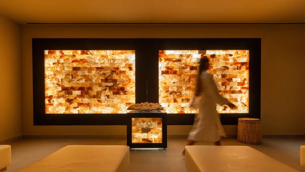 A guest in a robe walking past a glowing salt wall in a relaxation room