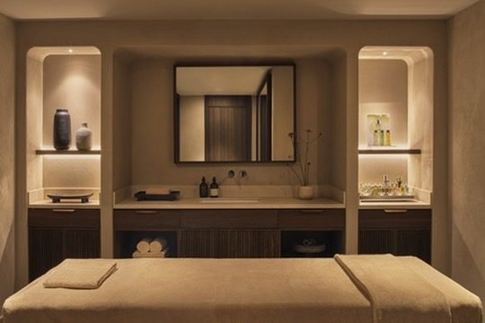 A calm treatment room with lit stone niches and a prepared massage bed